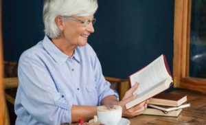 Літня жінка читає книжку й усміхається