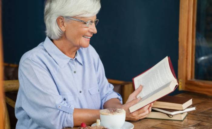 Літня жінка читає книжку й усміхається